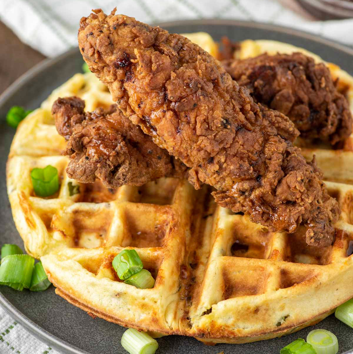 Fried chicken on a waffle with green onions on a gray plate.